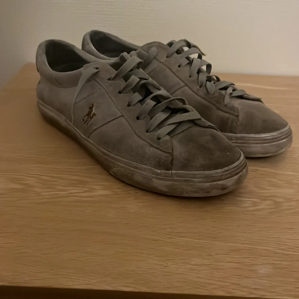 Säljer ett par grå sneakers från Polo i bra skick. De har en klassisk design med snörning och är tillverkade i skinn. Perfekta för vardagsbruk och passar till de flesta outfits. Sulan är i gummi och ger bra grepp. Lite slitna men fortfarande snygga och bekväma.. Skor.