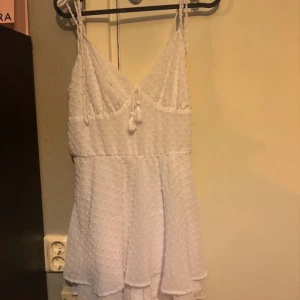 Vit  klänning med smala axelband - vit klänning med smala axelband. Klänningen har en v-ringad design och en luftig passform, perfekt för varma dagar men även kalla. Den har även en söt knytning framtill och en skitsnygg rygg. Helt ny