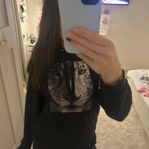 Svart hoodie med leopardtryck - Säljer en svart hoodie med ett coolt leopardtryck på framsidan. Perfekt för en avslappnad stil och passar bra till både jeans och mjukisbyxor. Den har långa ärmar och en klassisk huva med dragsko. Superbekväm och stilren!