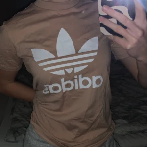 Beige t-shirt från Adidas - Säljer en beige t-shirt från Adidas med deras klassiska logga i vitt på bröstet. T-shirten är i bra skick och har en normal passform.