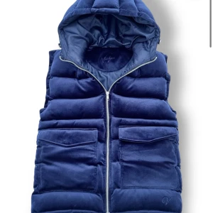 Mörkblå quiltad väst med huva - Säljer en snygg mörkblå vendiera väst med huva. Västen har en dragkedja framtill och stora fickor med lock. Perfekt för kyliga dagar och ger en cool look. Passar både till vardags och lite mer avslappnade tillfällen. Aldrig använd så skicket är 10/10. Säljer på grund av fel storlek 