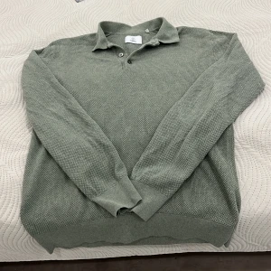 Grön pikétröja från Bläck - Säljer en stilren grön pikétröja från Bläck. Tröjan har en klassisk krage med knappar. Den är långärmad och är i storleken S