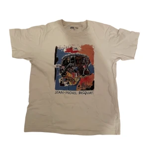 Vit uniqlo t-shirt  - Säljer en vit t-shirt från Uniqlo med ett coolt Jean-Michel Basquiat-tryck i flera färger. T-shirten har en klassisk passform och korta ärmar. Perfekt för konstälskare och streetwear-entusiaster.