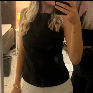  topp med knytning - Snygg svart ärmlös topp med knytning i ryggen. Man kan även ha tröjan bakåfram genom att ha knytningen där fram istället😍. Toppen har en elegant design med en öppen ryggdetalj. Använd 3 gånger ca.