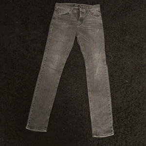 Grå jeans från Replay - Snygga grå jeans från Replay med klassisk femficksdesign och dragkedja. De har en straight passform och är perfekta för en avslappnad stil. Märkesdetaljer syns på både fram- och baksida.