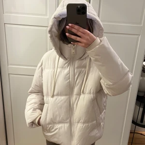 Pufferjacka med huva - Krämvit pufferjacka med huva och dragkedja. Jackan är quiltad och varm för vintern. Praktiska fickor framtill med drgkedjor. Köptes på Zara för 559kr, pris kan diskuteras. Använd fåtal gånger.