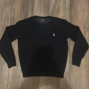 Mörkblå tröja från Ralph Lauren - Säljer en stilren mörkblå tröja från Ralph Lauren med det klassiska broderade logotypen på bröstet. Tröjan har långa ärmar och en rund halsringning. Perfekt för en avslappnad och elegant look. Storlek XS passar runt 160-170