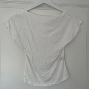 Vit topp med öppen rygg - Säljer en stilren vit topp med korta ärmar och en djup öppen rygg. Perfekt för varma dagar eller som ett lager under en jacka. Enkel och elegant design som passar till många olika outfits.