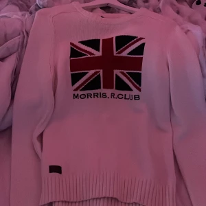 Vit tröja från Morris R. Club - Säljer en stilren vit tröja från Morris R. Club med ett stort Union Jack-motiv på framsidan. Tröjan har långa ärmar och ribbstickade muddar vid ärmslut och nederkant. Perfekt för en avslappnad och trendig look.