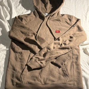 hoodie från Les Deux - Säljer en snygg brun/mörk grön hoodie från Les Deux med en liten röd broderad logga på bröstet. Tröjan har en en stilren design för avslappnade tillfällen. Säljer för att den är för liten. Skick:9,5/10