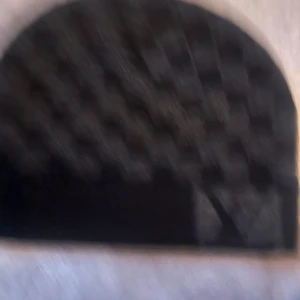 Svart handväska med rutigt mönster - Snygg svart handväska med ett diskret rutigt mönster. Perfekt för att ge en stilren touch till din outfit. Väskan har en halvcirkelformad design som gör den unik och trendig.