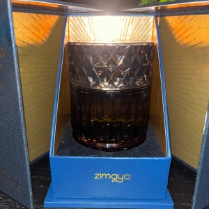 Sharaf the Club av Zimaya - Exklusiv parfym från Zimaya, Sharaf the Club, i en elegant flaska med diamantmönstrad design. Flaskan är placerad i en lyxig förpackning med guldtext och blå insida. Perfekt för den som söker en sofistikerad doftupplevelse.