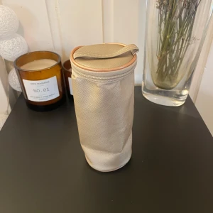 Beige cylinderformad necessär  - Säljer en beige cylinderformad necessär med dragkedja och handtag. Perfekt för att förvara småsaker eller sminkborstar. Enkel och praktisk design. 18cm lång, 8cm bred