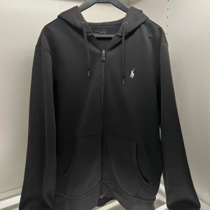 Ralph Lauren Zip hoodie - Säljer en stilren svart hoodie från Ralph med dragkedja och klassisk logga på bröstet, 100% äkta. Tröjan har långa ärmar och en praktisk huva. Perfekt för en avslappnad look. Endast Swish betalning! Kontakta mig om du har fler frågor eller vid betalning!