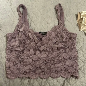 Lila spetslinne från Newyorker - Säljer ett lila spetslinne från Newyorker. Linnet har ett vackert blommigt spetsmönster och är ärmlöst med smala axelband. Perfekt för en somrig look!