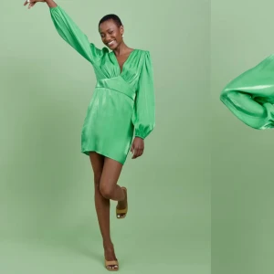 Grön klänning  - Snygg grön kortklänning i satin med v-ringning och långa puffärmar. Klänningen har en figursydd passform, den har en mjuk och glansig yta. Klänningen är aldrig använd och har prislappar kvar köptes för 499kr