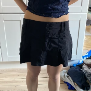 Svart kjol från H&M Divided - Snygg svart kjol från H&M Divided i storlek M. Kjolen har en kort längd och knappar framtill.