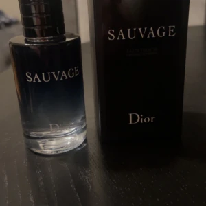 Sauvage Eau de Toilette från Dior - Säljer en flaska Sauvage Eau de Toilette från Dior. Flaskan är elegant med en mörkblå ton och har en stilren design. Perfekt för den som vill ha en fräsch och maskulin doft.