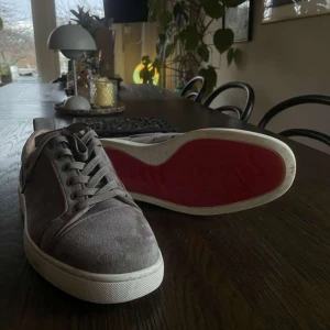 Loubs med röd sula  - Snygga grå Loubs  mocka med en ikonisk röd sula. Skorna har snörning och en stilren design som passar perfekt för en trendig look.