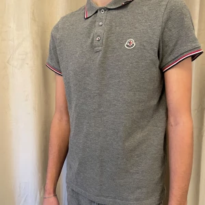 Moncler pikétröja  - Grå piké från Moncler i jätte fint skick. Köpt på NK för något år sedan och knappt använd sedan dess. Röda vita och blå detaljer