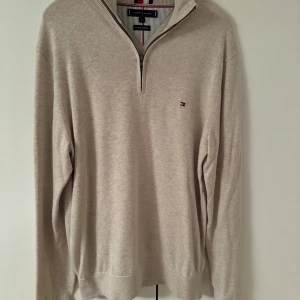 Beige tröja med dragkedja från Tommy Hilfiger - Säljer en stilren beige tröja från Tommy Hilfiger i premium bomull. Tröjan har en halv dragkedja och ett diskret logotypbroderi på bröstet. Perfekt för en avslappnad men snygg look.