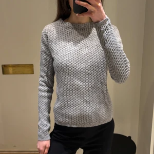 Grå stickad tröja från Stockh LM - Stilren grå stickad tröja från Stockh LM. Tröjan har en texturerad yta och långa ärmar, perfekt för kyligare dagar. Den är i storlek XS.