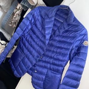 Blå dunjacka från Moncler - Snygg blå dunjacka från Moncler med quiltad design . Jackan har en klassisk krage och långa ärmar. Perfekt för kyligare dagar. Storlek 36/s 