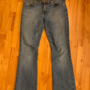 Levis bootcut jeans i blå denim - Snygga Levis Lågmidjade bootcut jeans i blå denim med femficksdesign. De är i storlek 38 och men de har en slitning på lappen där bak.