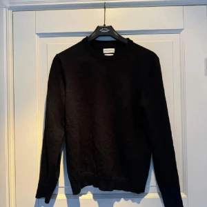 Svart tröja från These Glory Days - Säljer en stilren svart tröja från These Glory Days i Superior Merino. Tröjan har en klassisk rund hals och långa ärmar, perfekt för kyligare dagar. Den är mjuk och bekväm, vilket gör den till ett utmärkt val för både vardag och mer uppklädda tillfällen.