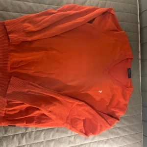 Orange tröja från Peak Performance - Säljer en snygg orange tröja från Peak Performance. Tröjan har en v-ringad design och långa ärmar med ribbade muddar. Perfekt för en stilren och bekväm look. Str L men passa M perfekt