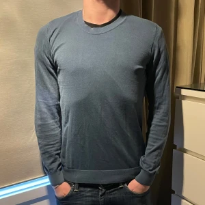 Blå tröja från Oscar Jacobson - Säljer en stilren blå tröja från Oscar Jacobson, tillverkad i Italien. Tröjan har en klassisk rund hals och långa ärmar, perfekt för en elegant och avslappnad look.