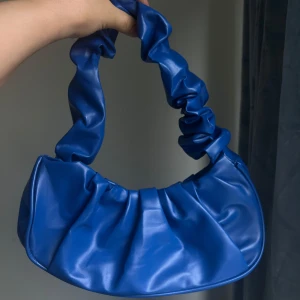 Blå axelväska med rynkad design - Snygg blå axelväska i syntetmaterial med en unik rynkad design. Perfekt för att ge din outfit en färgklick. Väskan har en stilren och modern look som passar till många tillfällen.