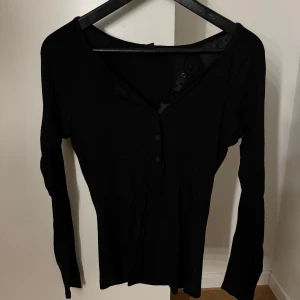 Svart långärmad topp från H&M - Svart långärmad topp från H&M med bruna/vinröda små knappar! Materialet är tunt, ribbat. Tröjan är i storlek 40-42/M i bra skick 🖤 Skriv för fler bilder 🫶🏼