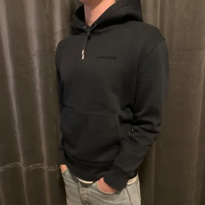 J. Lindeberg hoodie - Snygg hoodie från J.Lindeberg med justerbar dragsko i huvan och en praktisk magficka. Perfekt för en avslappnad stil. Diskret logotyp på bröstet ger en stilren look.