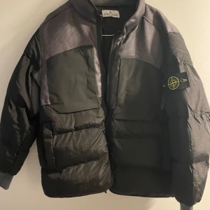 Stone Island puffer - Säljer en svart pufferjacka från Stone Island med en unik nylon metal/tyvek konstruktion. Jackan har en dragkedja framtill och en ikonisk logga på ärmen. Puffer med mesh från Stone Island. Använd en halv säsong sedan mest hängt i källaren. Storlek M mensens i storlekarna så en ganska normal S. Mycket fint skick. Alla lappar finns kvar och ligger i fickan. Passa på!  Insidan har två knappar för fäste av badgen om man vill gömma den.