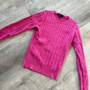 Rosa stickad tröja från GANT - Säljer en snygg rosa stickad tröja från GANT med kabelstickat mönster. Tröjan har långa ärmar och en rund halsringning. Perfekt för att hålla sig varm och stilren under kyligare dagar. 💖Storlek M