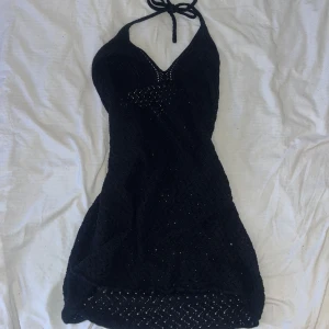 Svart stickad miniklänning  - Snygg svart stickad bikini med knytband i nacken. Den har en v-ringad design och ett fint mönster som ger en unik look. Perfekt för sommarens stranddagar.