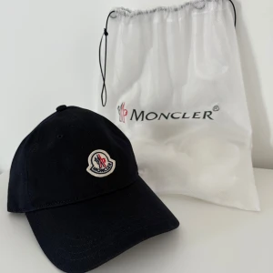 Mörkblå keps från Moncler - Snygg mörkblå keps från Moncler med broderad logotyp framtill. Perfekt för en stilren look. Kepsen är tillverkad i bomull och har en klassisk passform.