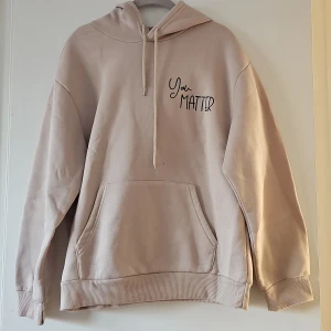 Beige hoodie från Shein - Säljer en beige hoodie från Shein med texten 'You Matter' på framsidan och ett inspirerande meddelande på baksidan. Hoodien har en stor ficka framtill och en bekväm passform. Perfekt för en avslappnad stil.