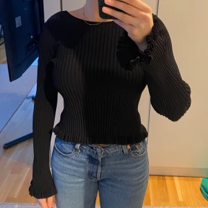 Svart ribbad topp med öppen rygg - Använd 1 gång. Svart ribbad figursydd topp med djup rygg och utsvängda ärmar med volangdetaljer. 
