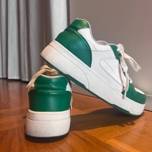 Vita och gröna sneakers - Snygga vita sneakers med gröna detaljer och snörning. Perfekta för en avslappnad stil. Skorna har en klassisk design med en tjock sula för extra komfort. Nypris 500kr. Använda ett fåtal gånger.