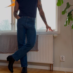 Blå jeansbyxor - Säljer ett par klassiska blå jeansbyxor med rak passform från wrangler med cowboy cut modellen.  De har en traditionell femficksdesign och en knappgylf. Perfekta för en avslappnad stil. Slitage på en av sidorna, går säkert att fixa på något sätt.