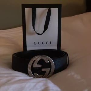 Svart bälte från Gucci - Snyggt svart bälte från Gucci med en stor silverfärgad GG-logotyp som spänne. Tillverkat i skinn med en elegant textur. Perfekt för att ge en lyxig touch till din outfit. Kommer med originalförpackning.