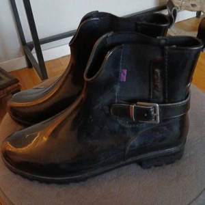 Svarta boots/gummistövlar från Tom Tailor - Snygga svarta boots från Tom Tailor med dekorativt bälte och spänne på sidan. Perfekta för höst och vinter med en stilren design. Stl 42