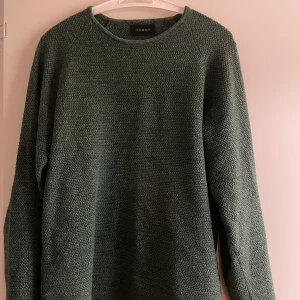 Grön stickad tröja från Gabba - Säljer en stilren grön stickad tröja från Gabba. Tröjan har en rund halsringning och långa ärmar, perfekt för kyligare dagar. Den har en enkel och klassisk design som passar till det mesta. Perfekt för både vardag och avslappnade tillfällen.