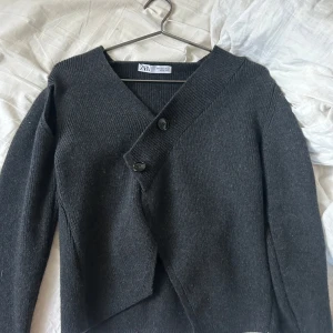 Mörkgrå omlottkofta från Zara - Säljer en stilren mörkgrå kofta från Zara. Koftan har en unik design med knappar framtill och långa ärmar. Perfekt för kyligare dagar och kan enkelt matchas med olika outfits. Ändats använd 3 gånger 💕Nypris: 599