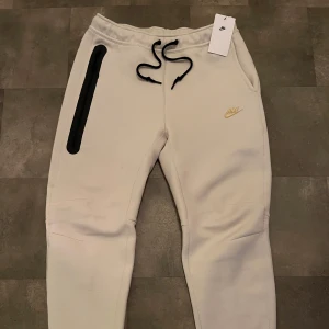 Beige mjukisbyxor från Nike -  Helt nya mjukisbyxor. Allsååå (oanvända)”Snygga beige mjukisbyxor från Nike med svart snörning och en diskret logga. Byxorna har en dragkedja på sidan och är perfekta för en avslappnad stil. Vill ni ha mer information så skriv personligt meddelande.