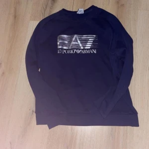 Mörkblå tröja från Emporio Armani - Snygg mörkblå tröja från Emporio Armani med deras ikoniska logga på bröstet. Perfekt för en stilren look. Tröjan har långa ärmar och en klassisk passform. Finns dock ingen skötselråds lapp