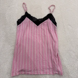 Rosa och svart randig linnetopp med spetsdetaljer - Säljer en söt rosa och svart randig linnetopp med smala axelband och spetsdetaljer vid halsringningen.