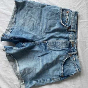 Snygga jeansshorts från Ginatricot - Säljer ett par klassiska blå jeansshorts från Ginatricot. Köpte de second hand, endast använt de några fåtal gånger. De har en avslappnad passform med medvetna slitna detaljer.